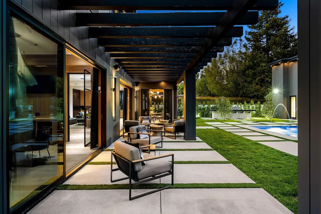 Luxury outdoor patio with pergola, modern lounge chairs, and a poolside garden setting at dusk